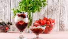 Dessert in vase and goblet with strawberries, blueberries, mint, cherries side view on pink and grungy background