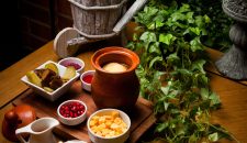 From above piti with crackers and pomegranate seeds and pickles in clay jug on wooden background