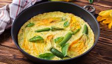 Oven baked omelette with flowers zucchini in  pan on wooden  background.